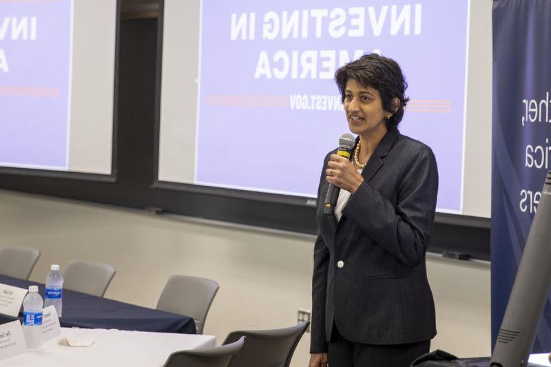 Chancellor Pyati holds microphone in front of signage reading "Investing in America"